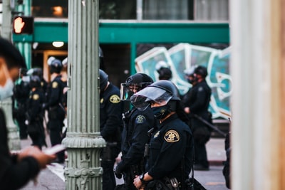 白天，一名身穿黑色警服的男子站在白色水泥柱附近